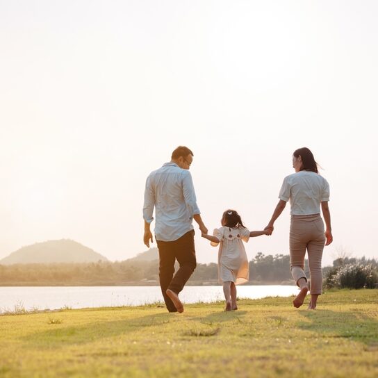 A young girl walks between her parents and holds their hands.