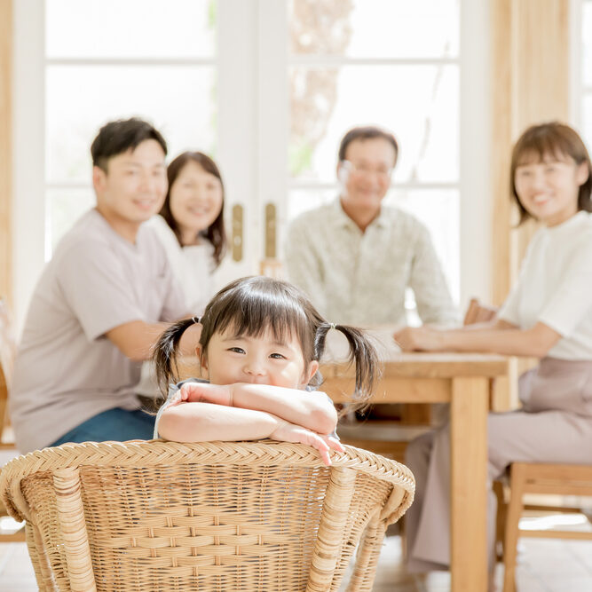 A three generation family sits at the kitchen table while young girl smiles at camera.