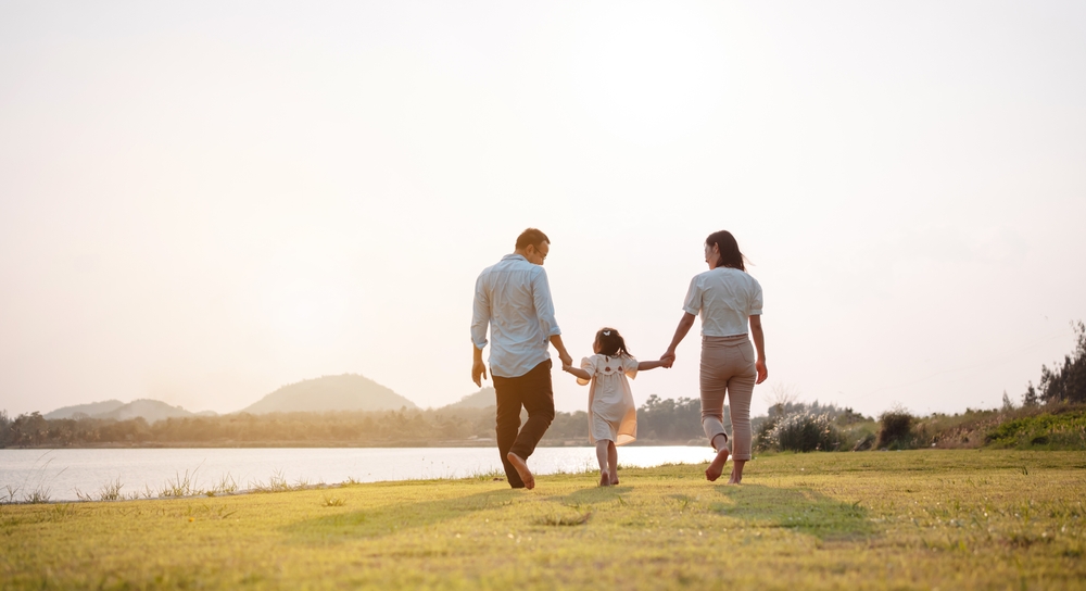 A young girl walks between her parents and holds their hands.