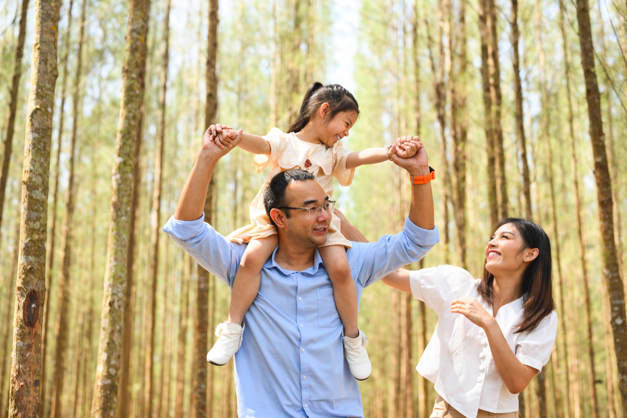 A happy family in the forest with daughter on father's shoulders.