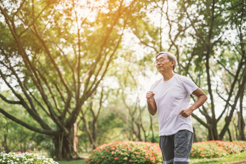 A male runs in a garden and forested area.