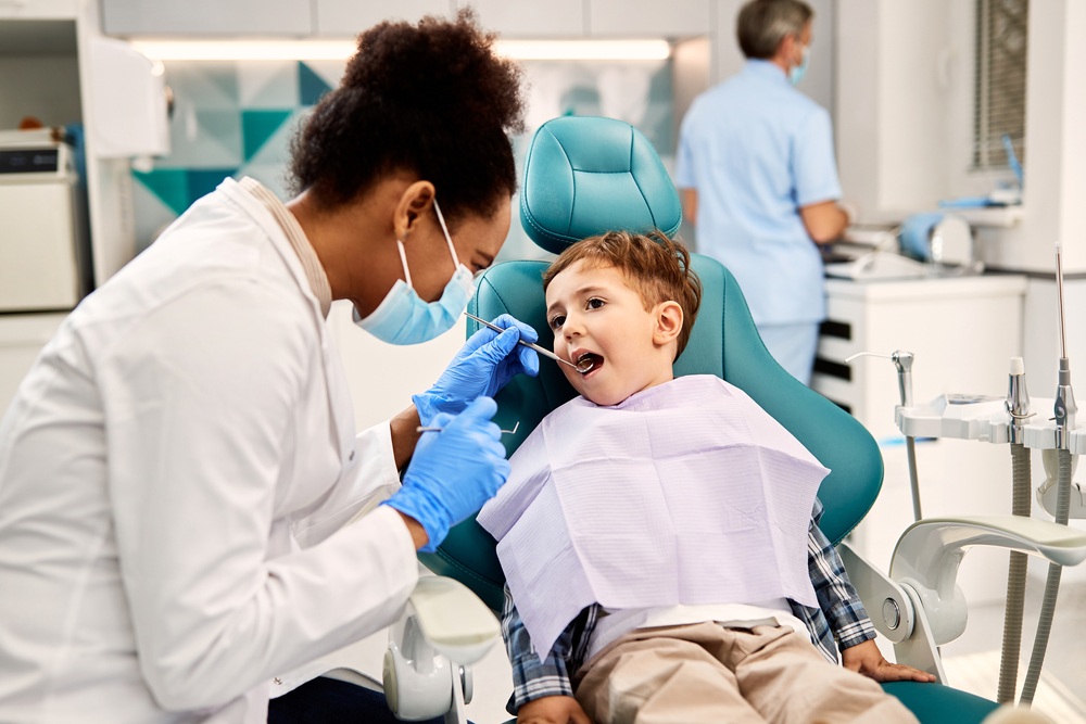 Black,Female,Dentist,Examining,Small,Boy's,Teeth,During,Dental,Procedure